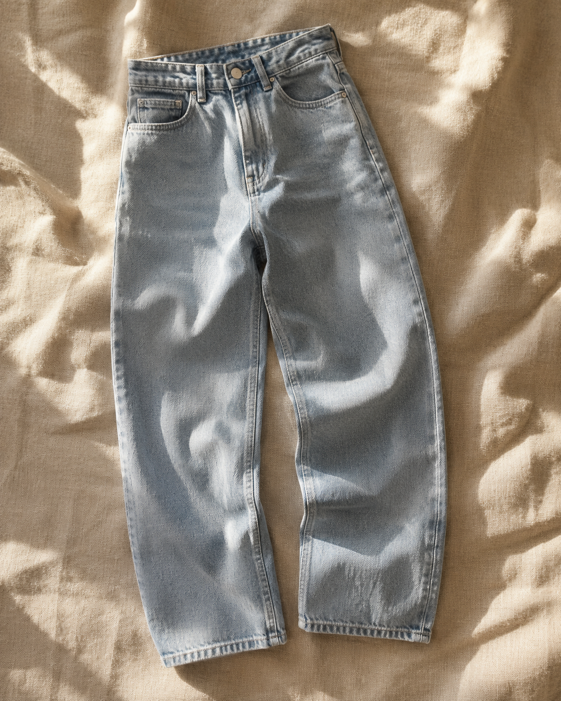 Premium light wash baggy jeans laid flat on beige linen fabric with soft natural sunlight, luxury contemporary denim fashion category image